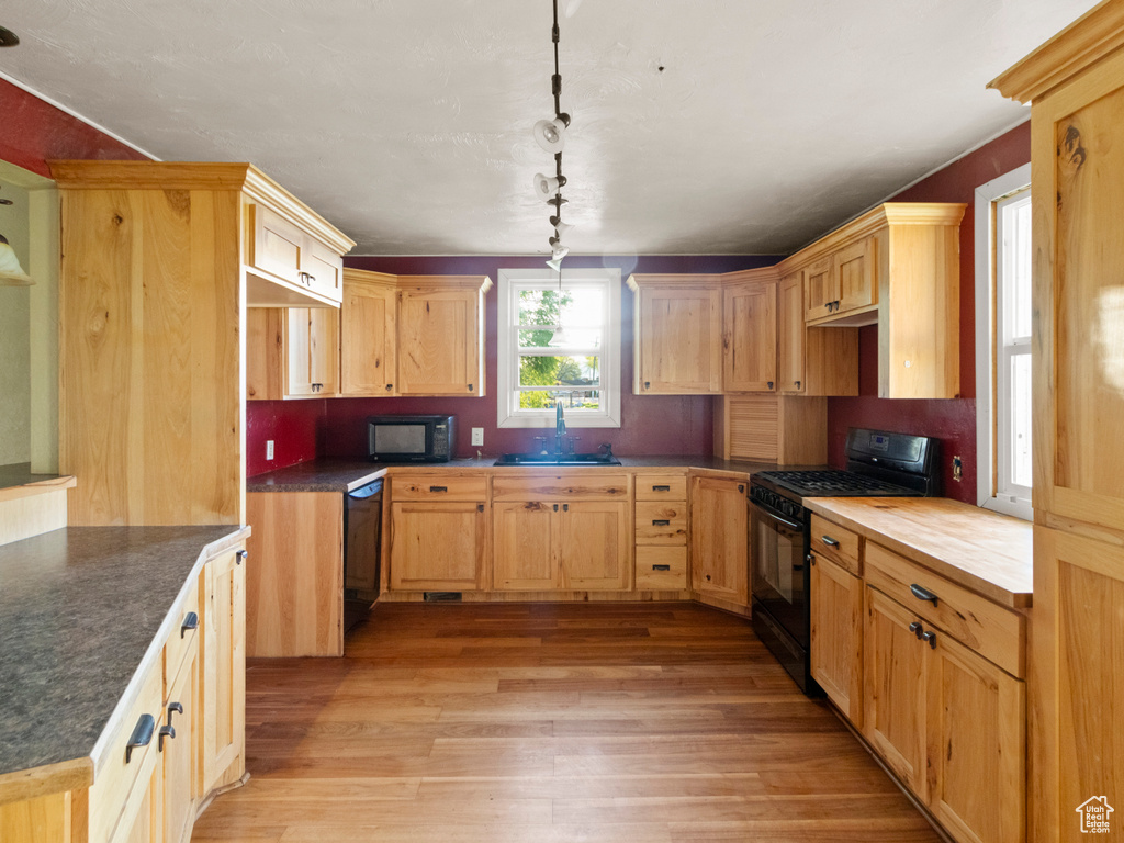 Kitchen featuring black appliances, light wood-style floors, light brown cabinets, and hanging light fixtures