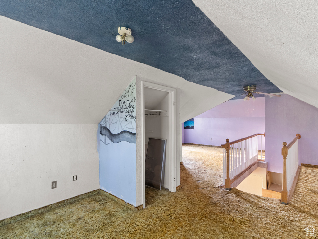 Additional living space with carpet, vaulted ceiling, a textured ceiling, and ceiling fan