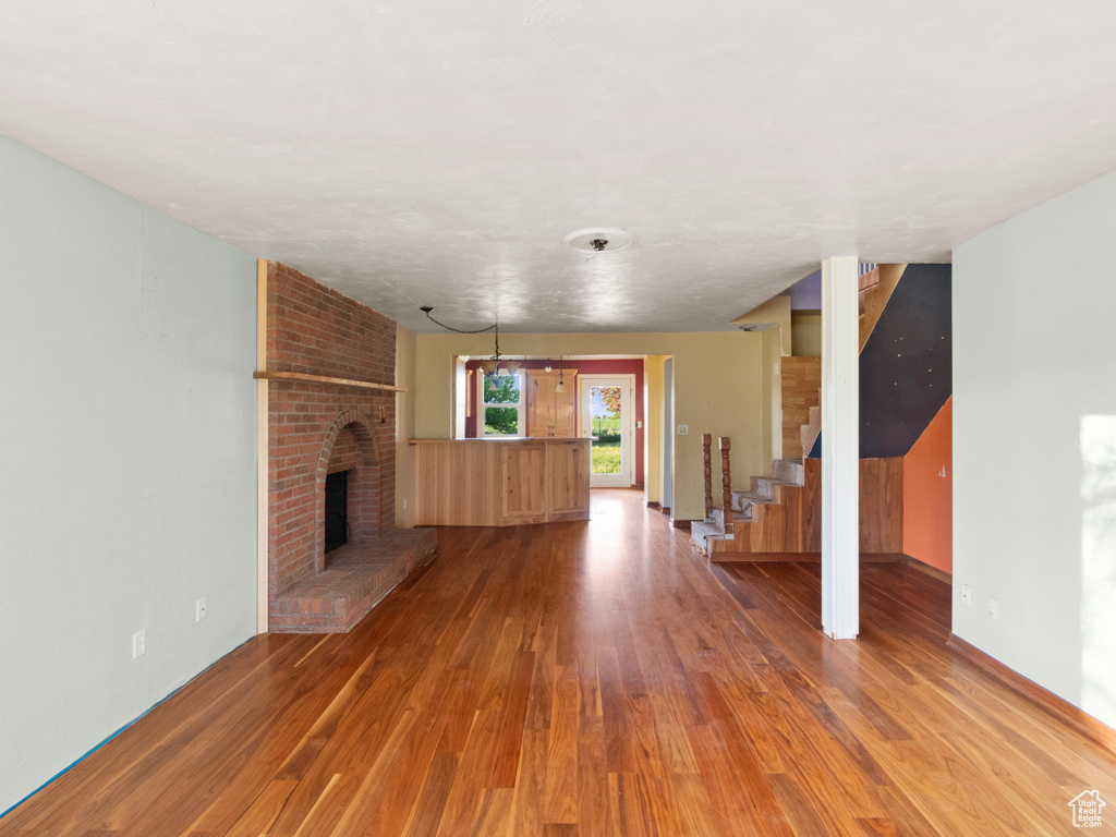 Unfurnished living room featuring wood finished floors, stairs, a brick fireplace, and baseboards