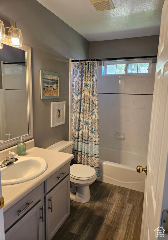 Full bathroom featuring wood finished floors, vanity, toilet, shower / bath combo, and a textured ceiling