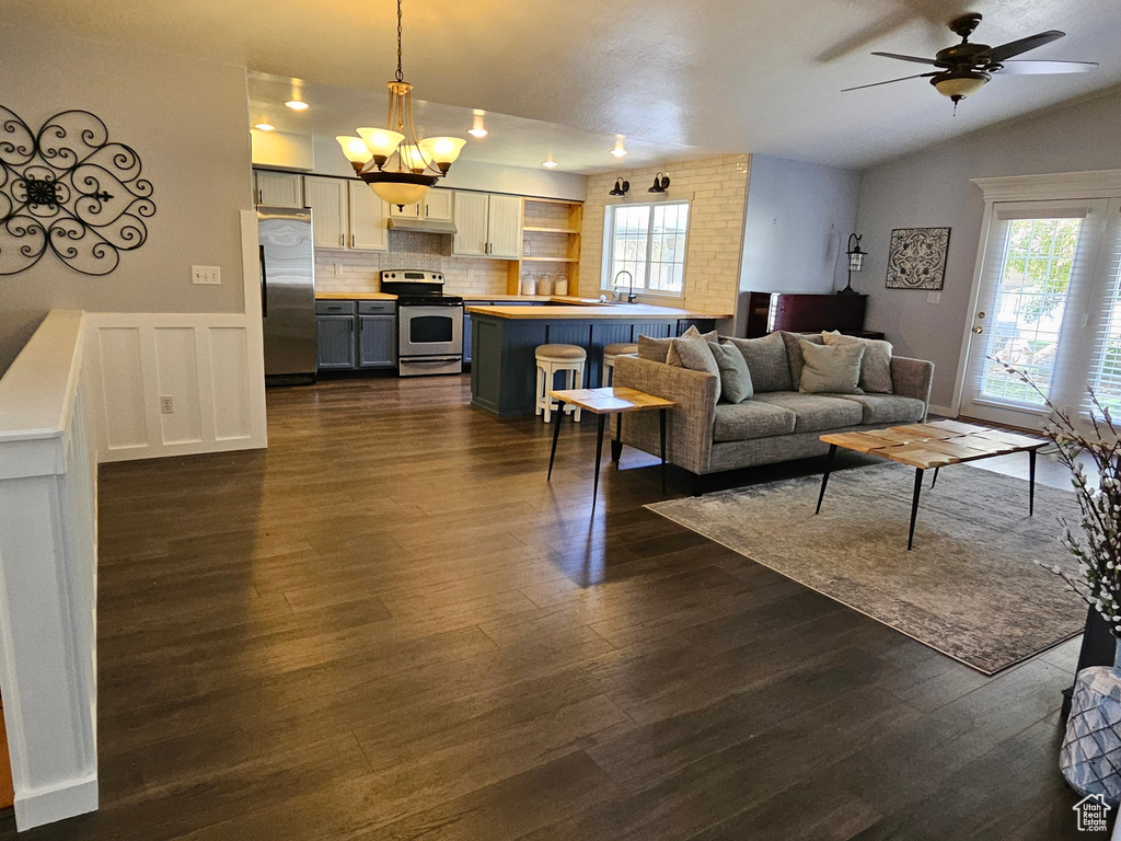 Living area with dark wood finished floors, a ceiling fan, lofted ceiling, and wainscoting