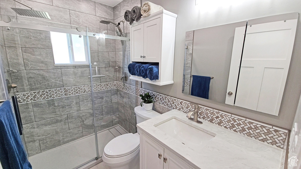 Full bathroom with a stall shower, toilet, vanity, backsplash, and tile walls