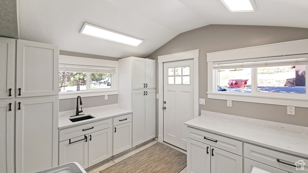Kitchen with vaulted ceiling, a sink, and white cabinetry