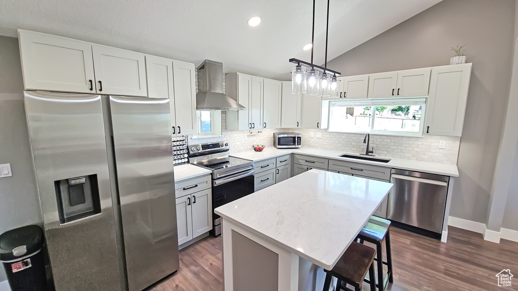 Kitchen with appliances with stainless steel finishes, wall chimney exhaust hood, a sink, tasteful backsplash, and a breakfast bar