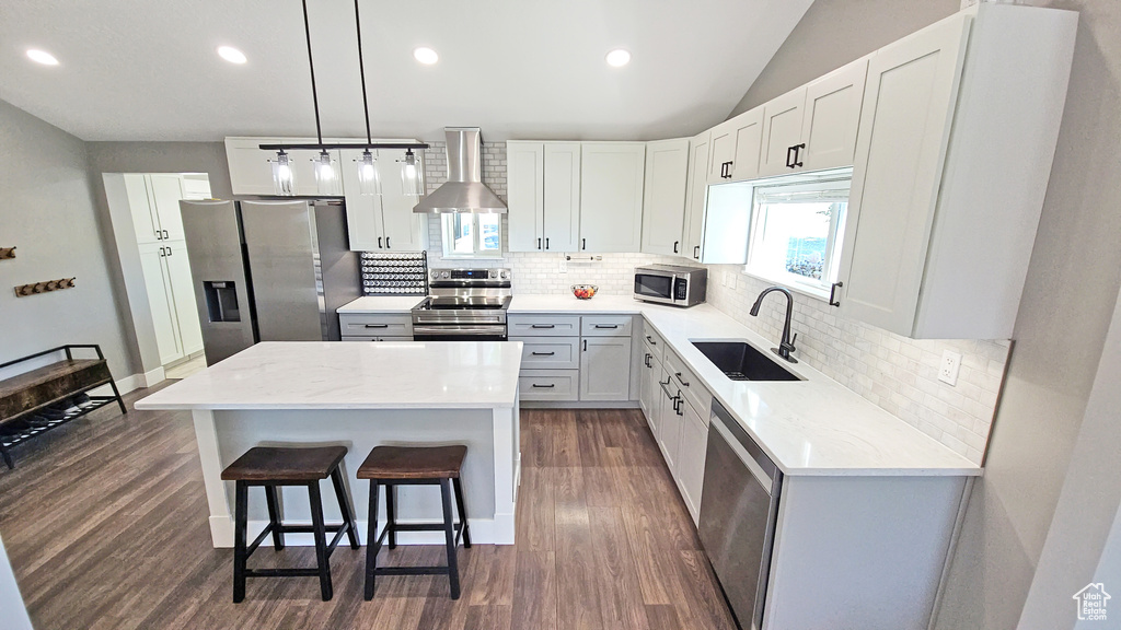 Kitchen with stainless steel appliances, wall chimney range hood, a sink, dark wood-style floors, and backsplash