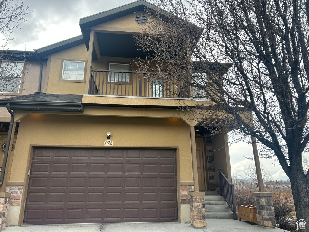 View of front of property featuring stucco siding, a balcony, and an attached garage