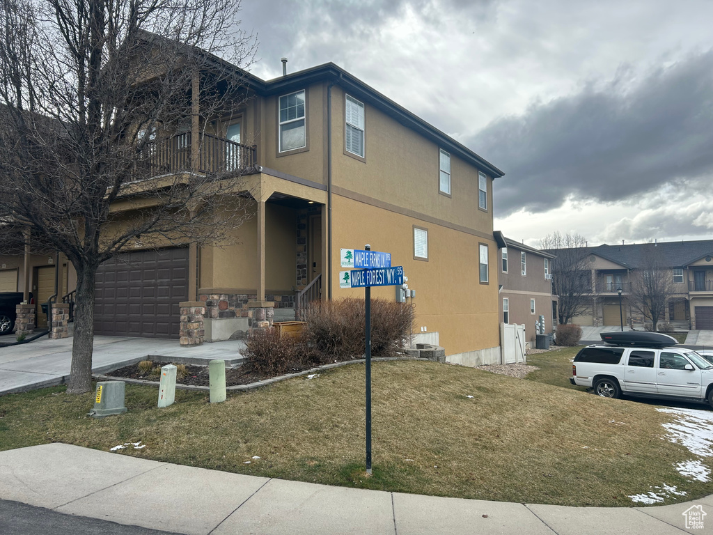 View of side of home with a balcony, a garage, concrete driveway, stucco siding, and a lawn