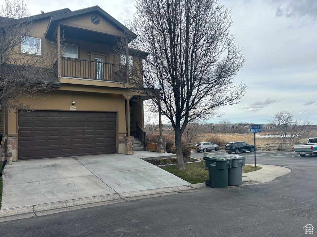 View of side of home featuring a balcony, stucco siding, an attached garage, and driveway