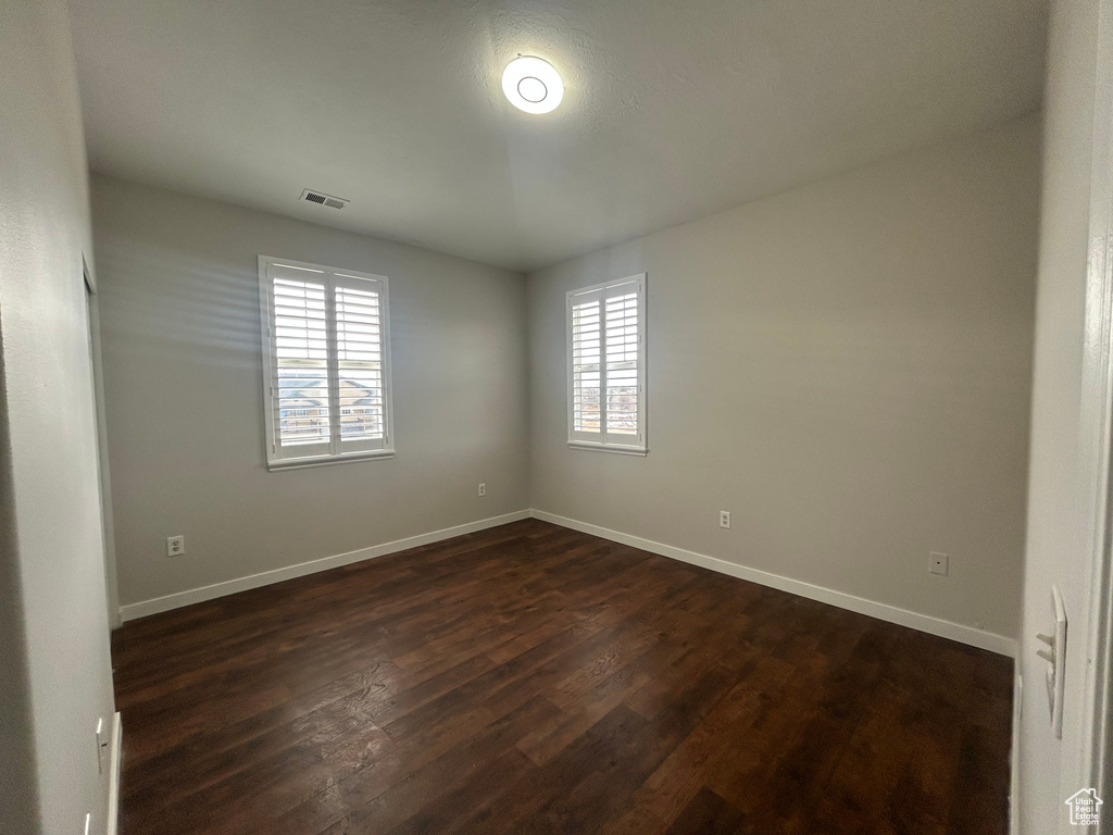 Spare room featuring healthy amount of natural light, dark wood-type flooring, and baseboards