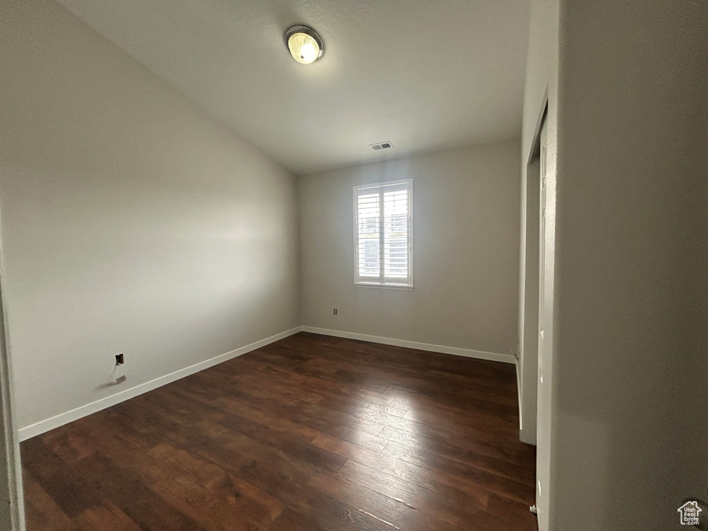 Spare room with dark wood-type flooring, vaulted ceiling, and baseboards