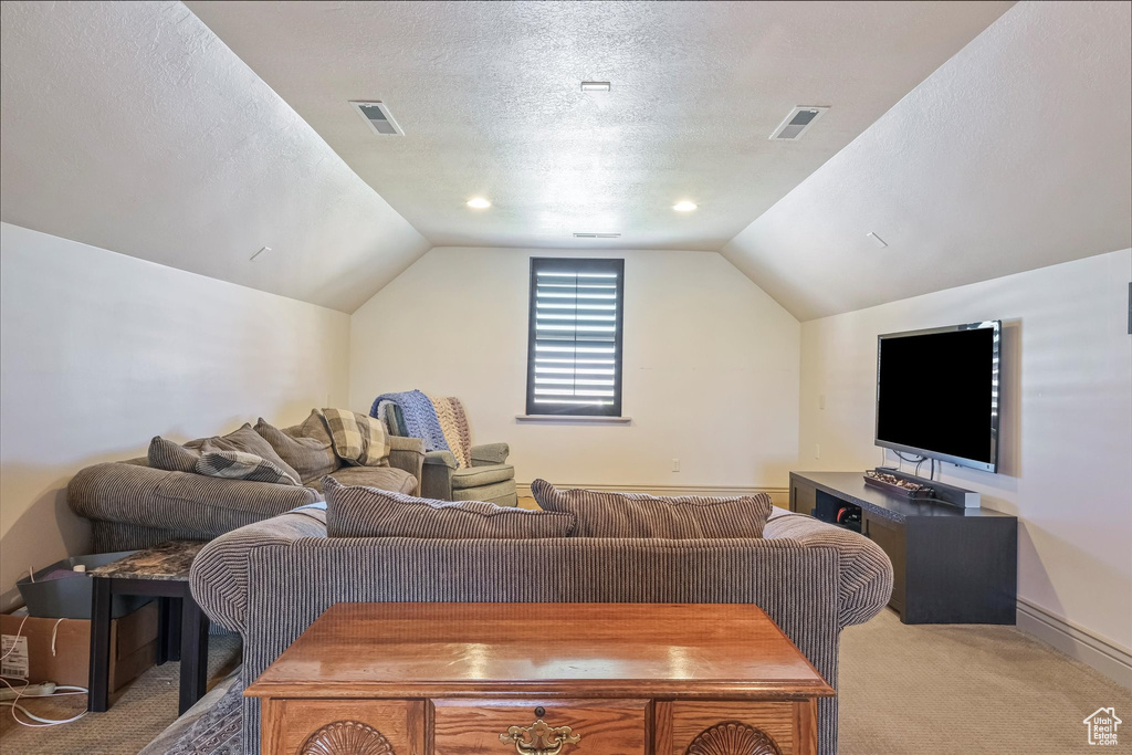 Living room featuring light colored carpet, lofted ceiling, a textured ceiling, and baseboards