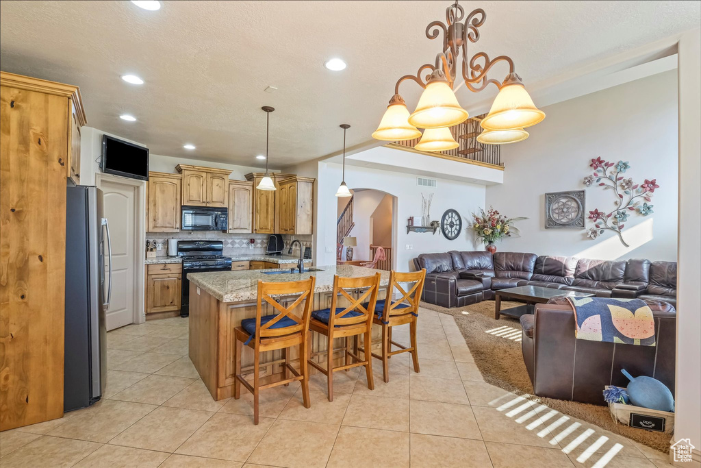 Kitchen with black appliances, arched walkways, open floor plan, light tile patterned floors, and a breakfast bar
