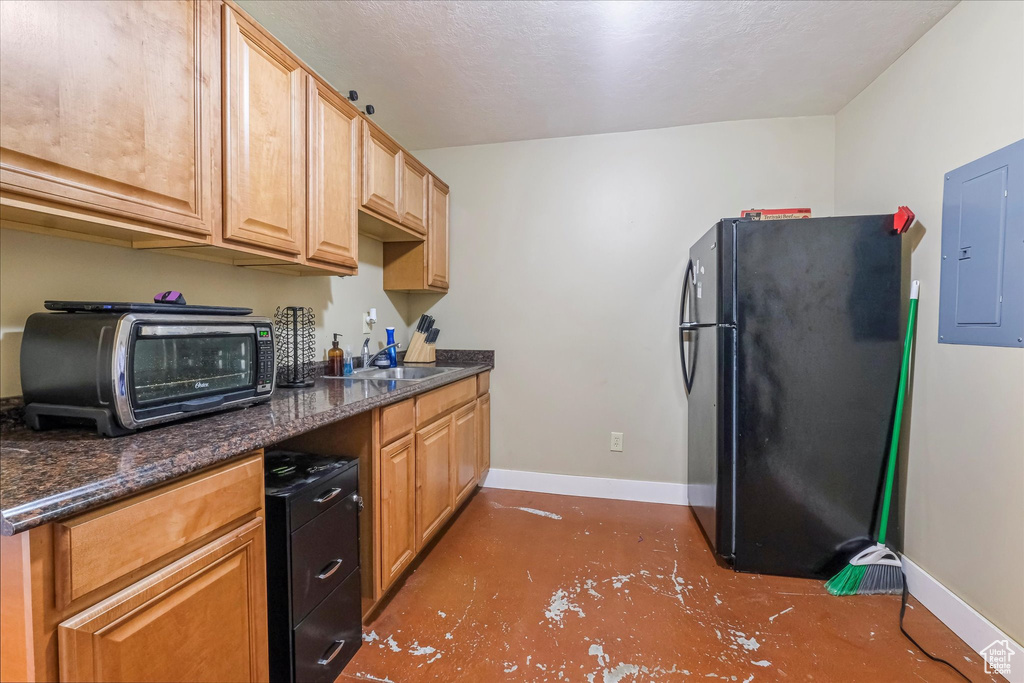 Kitchen featuring freestanding refrigerator, electric panel, a sink, baseboards, and concrete floors