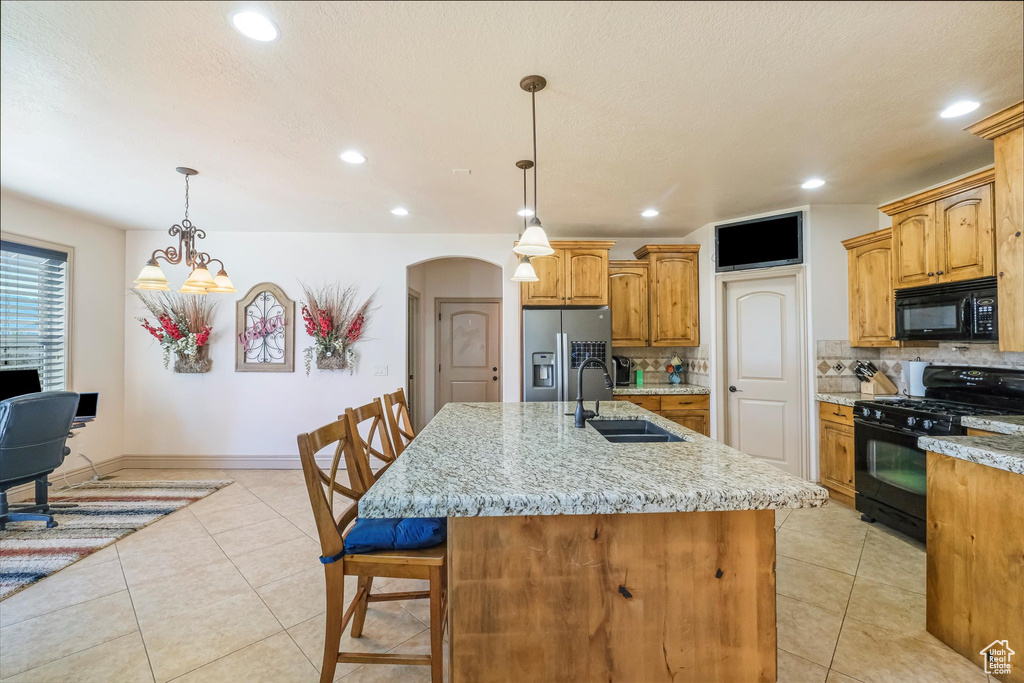 Kitchen featuring black appliances, a sink, arched walkways, tasteful backsplash, and a breakfast bar