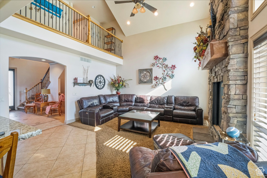 Living room featuring light tile patterned floors, ceiling fan, arched walkways, stairs, and high vaulted ceiling