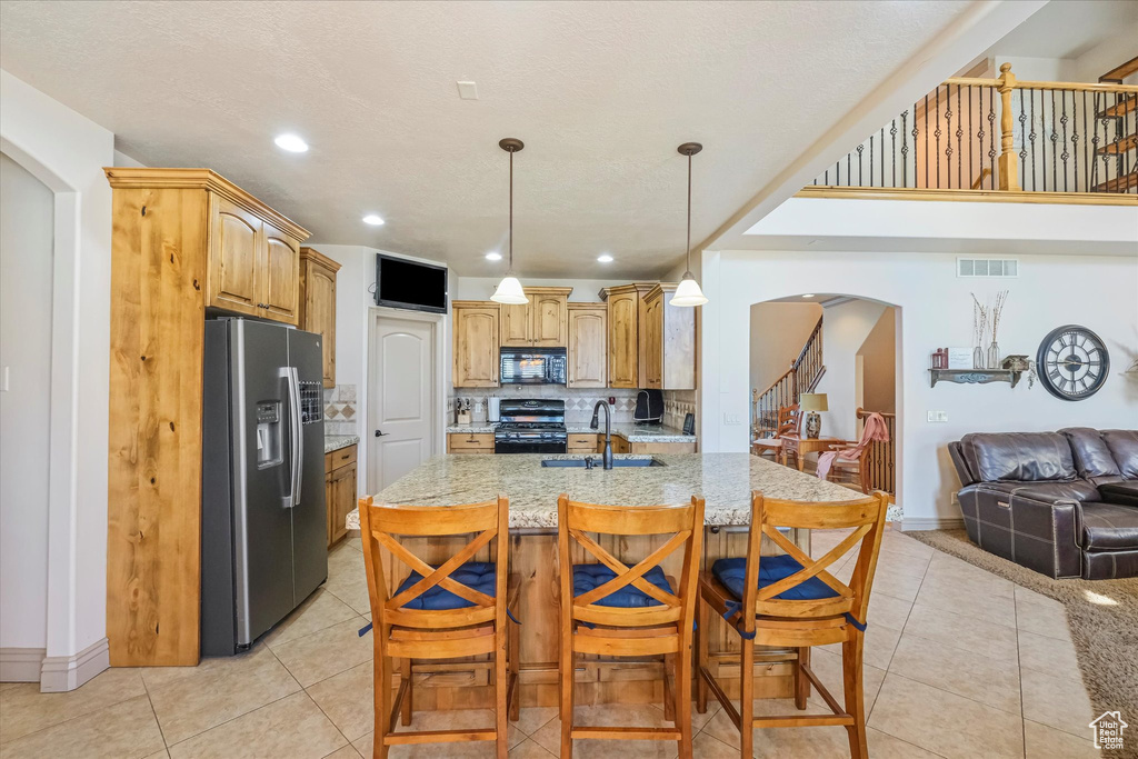 Kitchen featuring black appliances, arched walkways, light stone countertops, a sink, and open floor plan