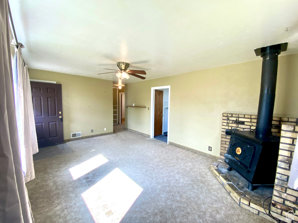 Unfurnished living room with carpet flooring, a wood stove, ceiling fan, and baseboards