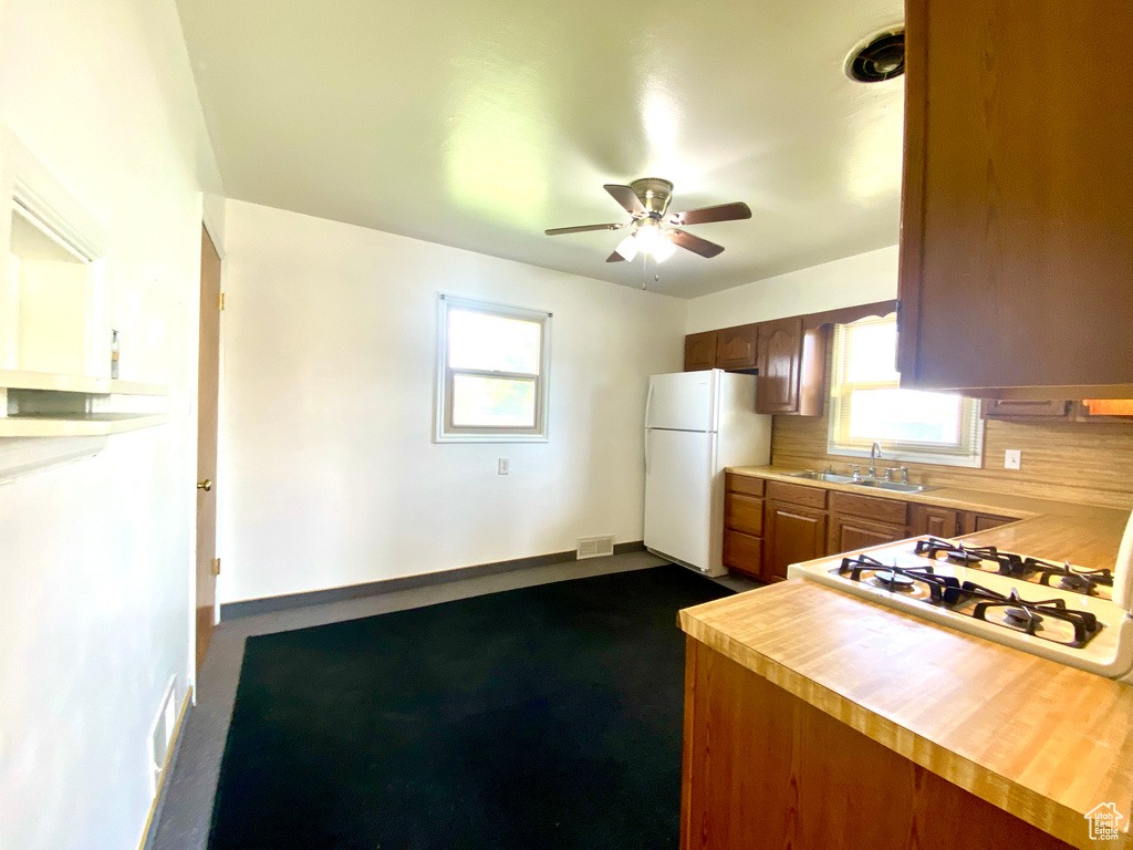 Kitchen with freestanding refrigerator, a sink, a ceiling fan, cooktop, and tasteful backsplash