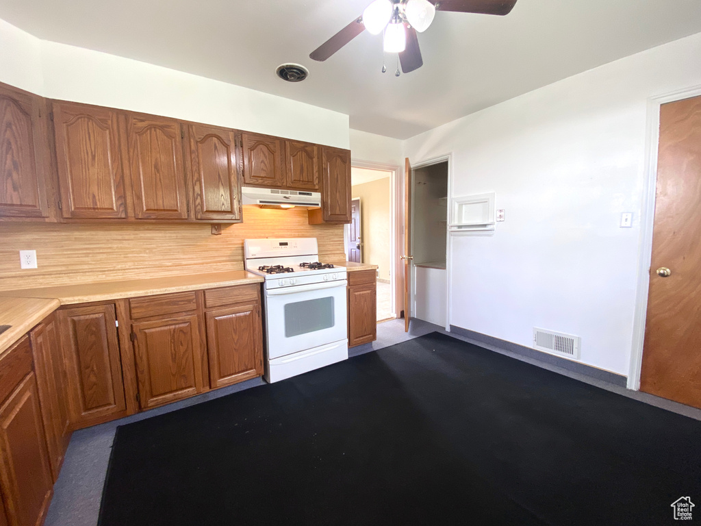 Kitchen with white gas range oven, under cabinet range hood, light countertops, and a ceiling fan