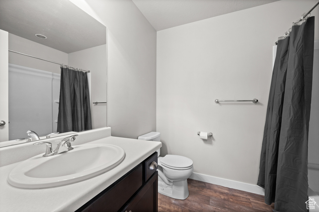 Bathroom featuring wood finished floors, baseboards, toilet, vanity, and a shower with shower curtain