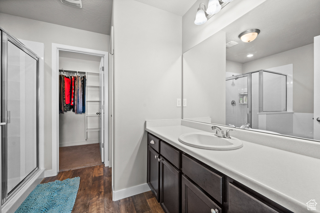 Bathroom featuring wood finished floors, a stall shower, baseboards, and a walk in closet