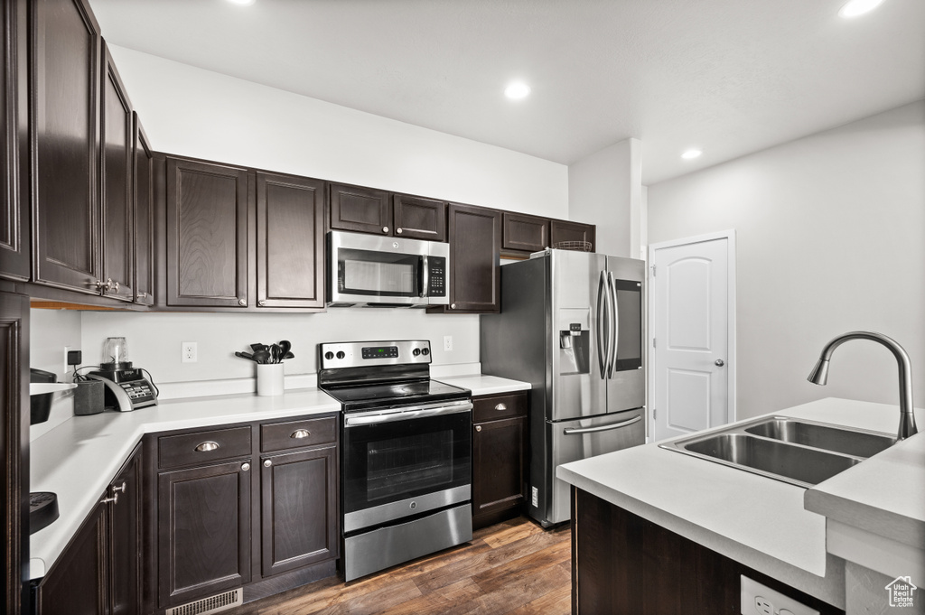 Kitchen featuring appliances with stainless steel finishes, a sink, dark wood-style flooring, recessed lighting, and dark brown cabinets