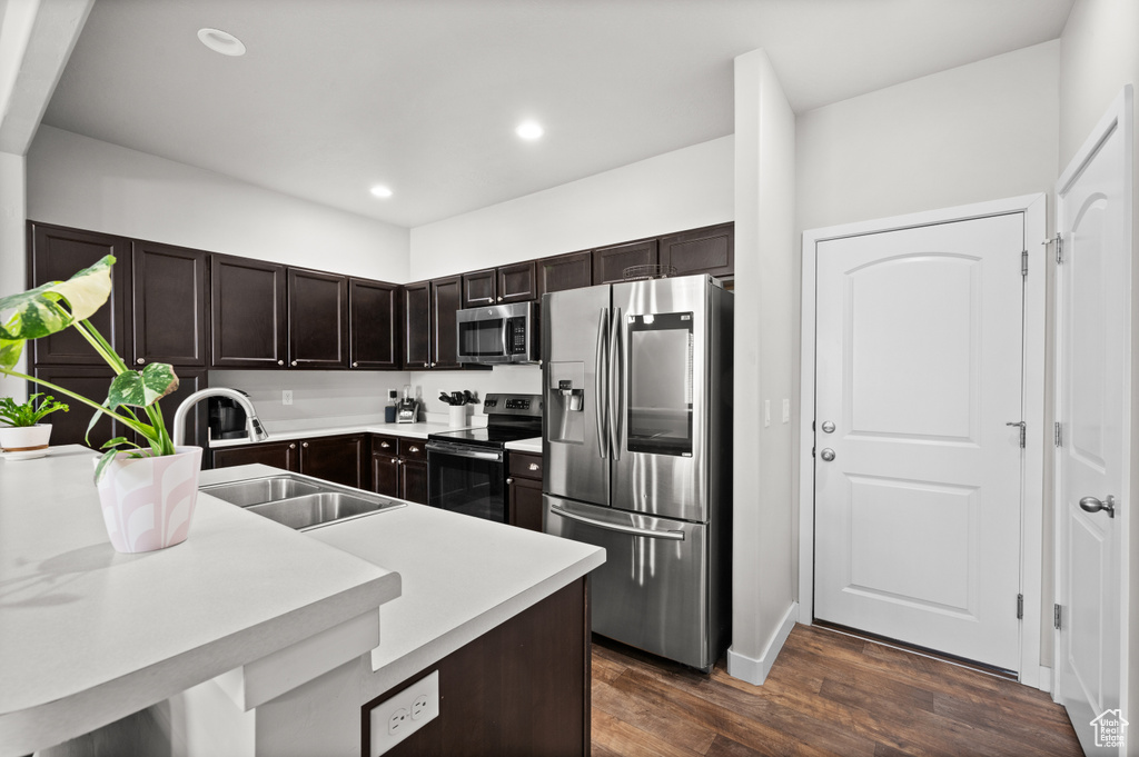 Kitchen featuring appliances with stainless steel finishes, a sink, dark brown cabinets, dark wood-style flooring, and light countertops