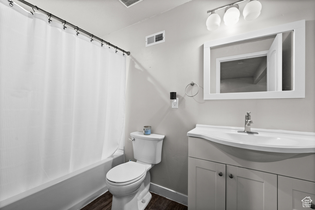 Bathroom featuring wood finished floors, toilet, baseboards, vanity, and shower / tub combo with curtain