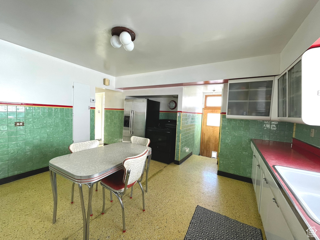 Kitchen featuring a sink, a wainscoted wall, white cabinets, glass insert cabinets, and stainless steel fridge with ice dispenser