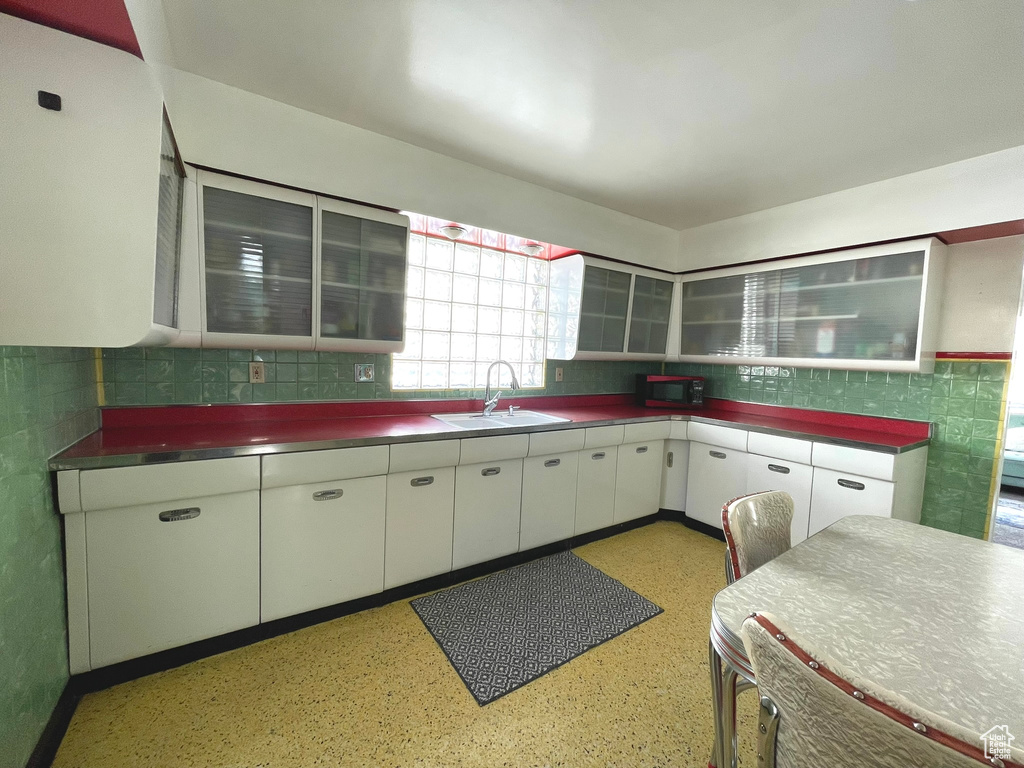 Kitchen featuring a sink, white cabinetry, glass insert cabinets, tile walls, and backsplash