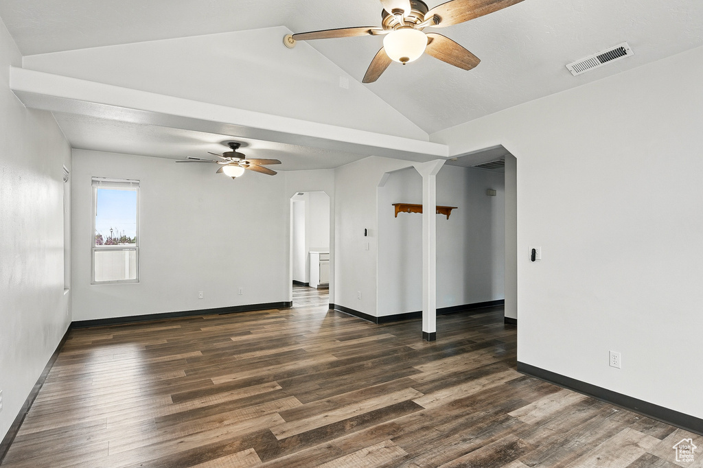 Spare room featuring a ceiling fan, arched walkways, vaulted ceiling, dark wood-type flooring, and baseboards