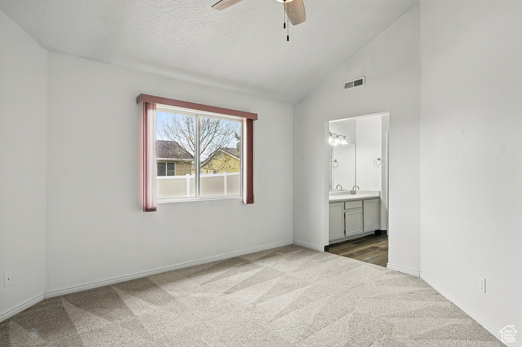 Unfurnished bedroom featuring carpet, baseboards, vaulted ceiling, ensuite bath, and ceiling fan