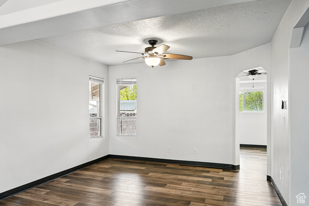Spare room featuring a ceiling fan, plenty of natural light, dark wood-type flooring, and a textured ceiling