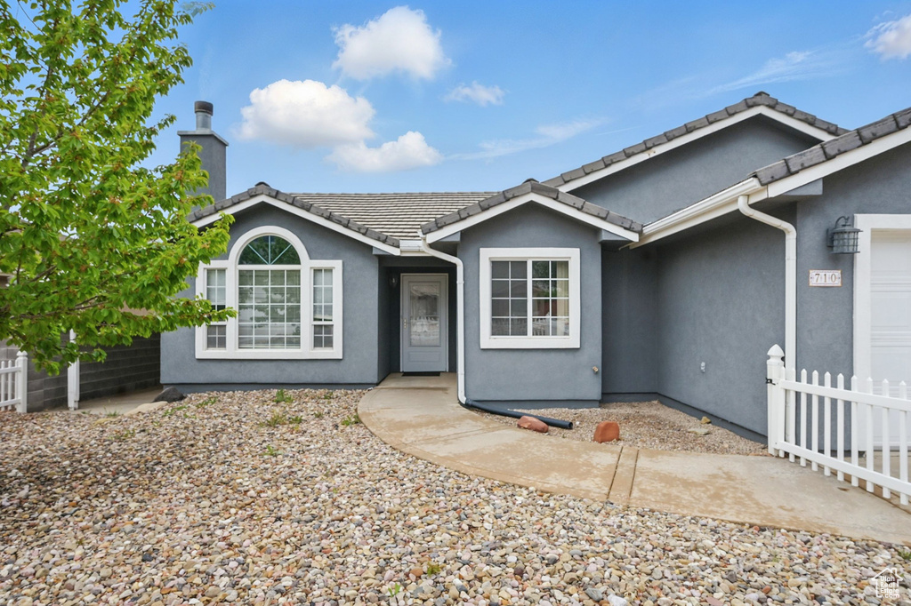 Ranch-style home featuring fence, stucco siding, a chimney, and a tile roof