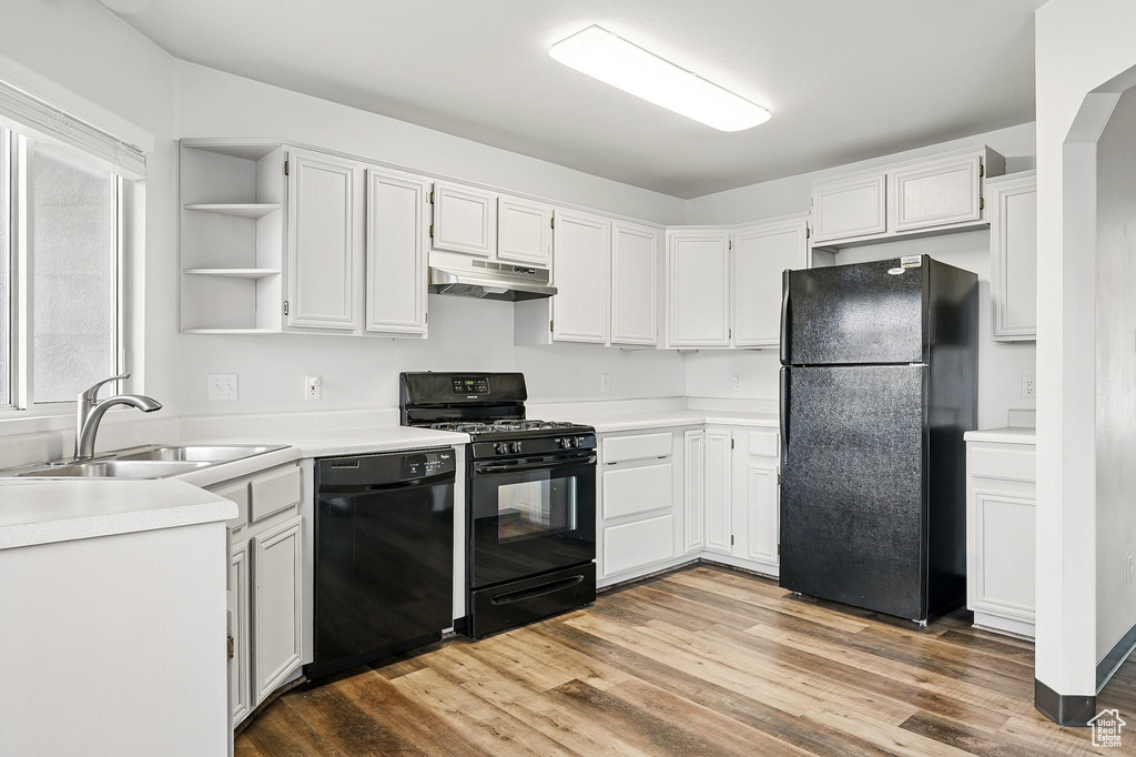Kitchen featuring black appliances, a sink, under cabinet range hood, open shelves, and light wood-style flooring