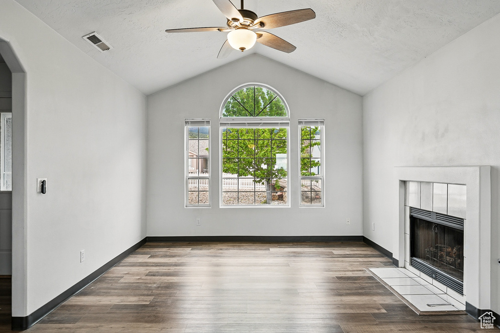 Unfurnished living room with ceiling fan, a tiled fireplace, vaulted ceiling, arched walkways, and wood finished floors