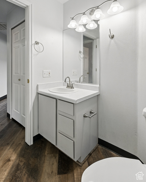 Half bath featuring wood finished floors, vanity, toilet, and baseboards