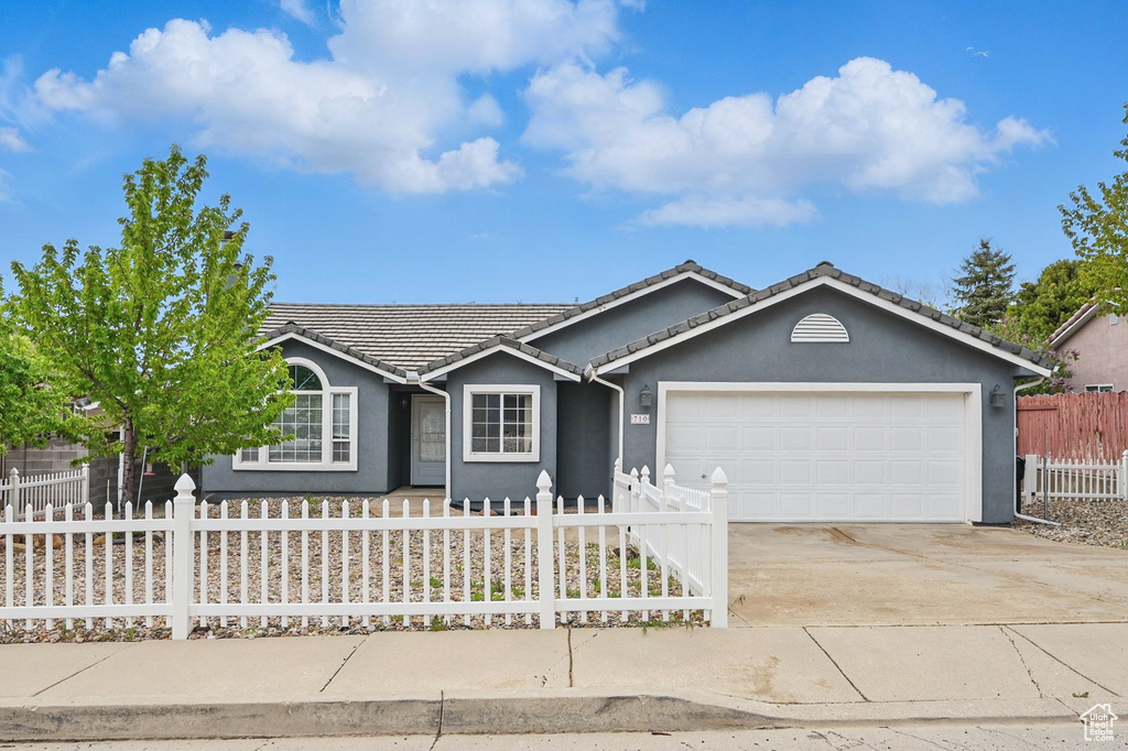Single story home with a fenced front yard, an attached garage, driveway, stucco siding, and a tiled roof