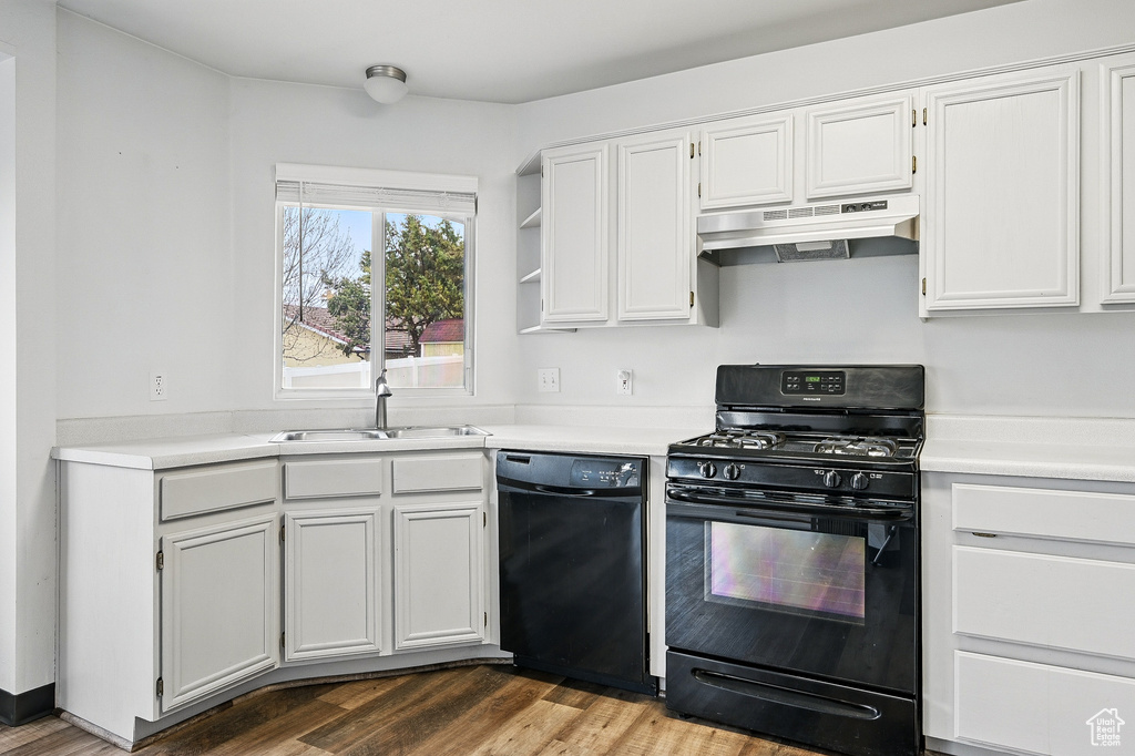 Kitchen with black appliances, under cabinet range hood, a sink, light countertops, and wood finished floors