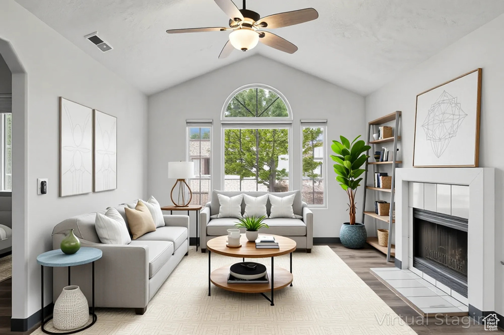 Living room with wood finished floors, ceiling fan, a tiled fireplace, lofted ceiling, and arched walkways