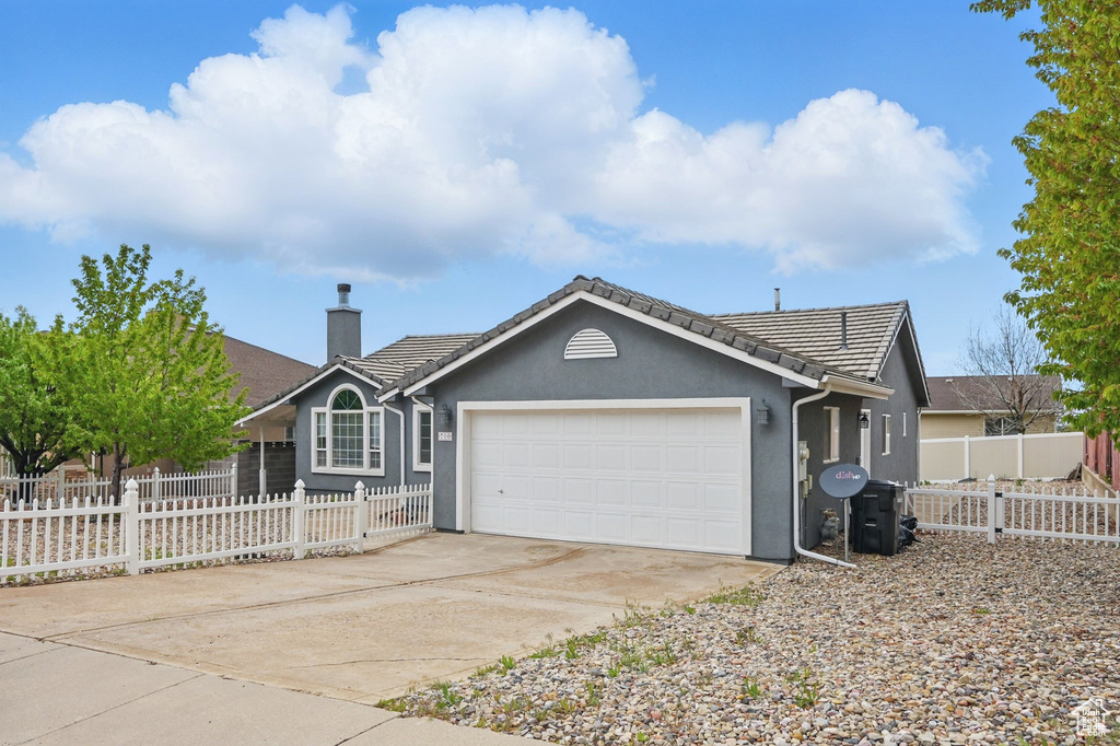 Ranch-style house featuring a garage, a chimney, driveway, and a tile roof