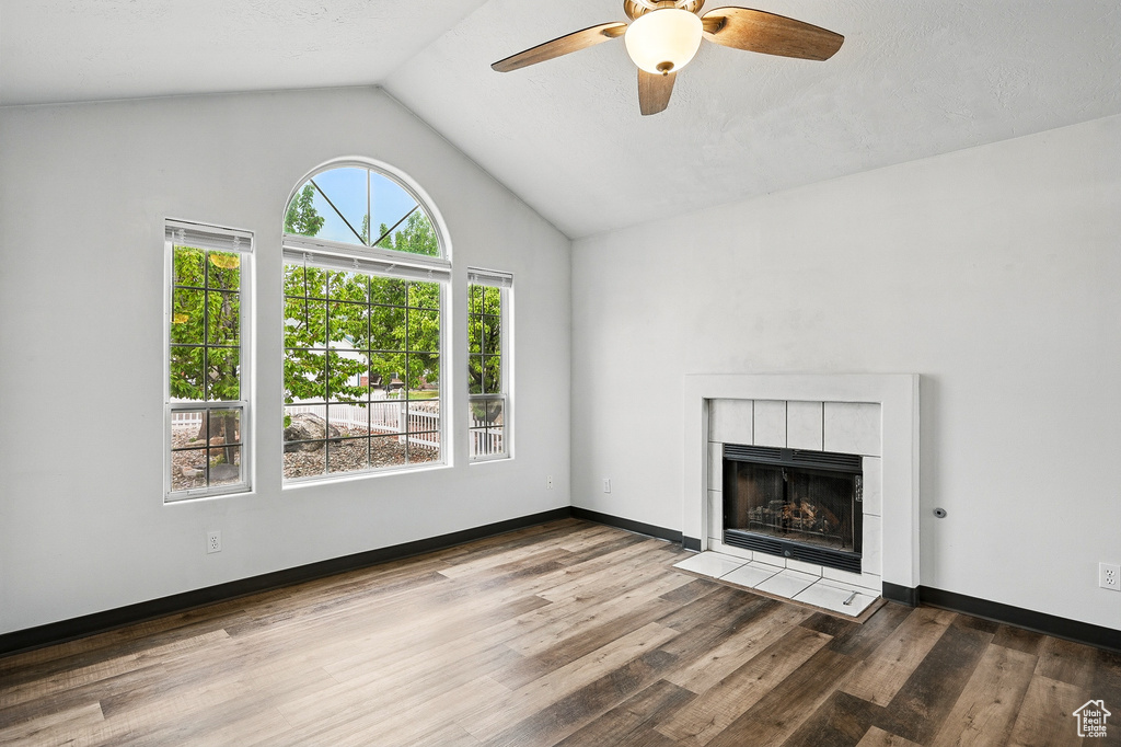 Unfurnished living room with a ceiling fan, wood finished floors, a tile fireplace, high vaulted ceiling, and baseboards