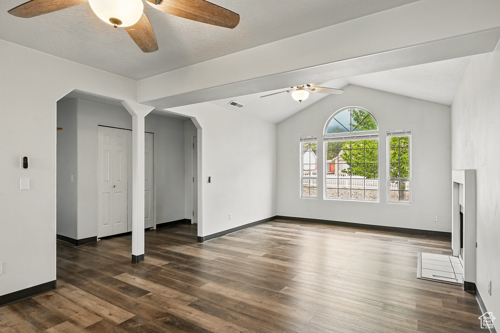 Unfurnished living room featuring arched walkways, ceiling fan, wood finished floors, and vaulted ceiling