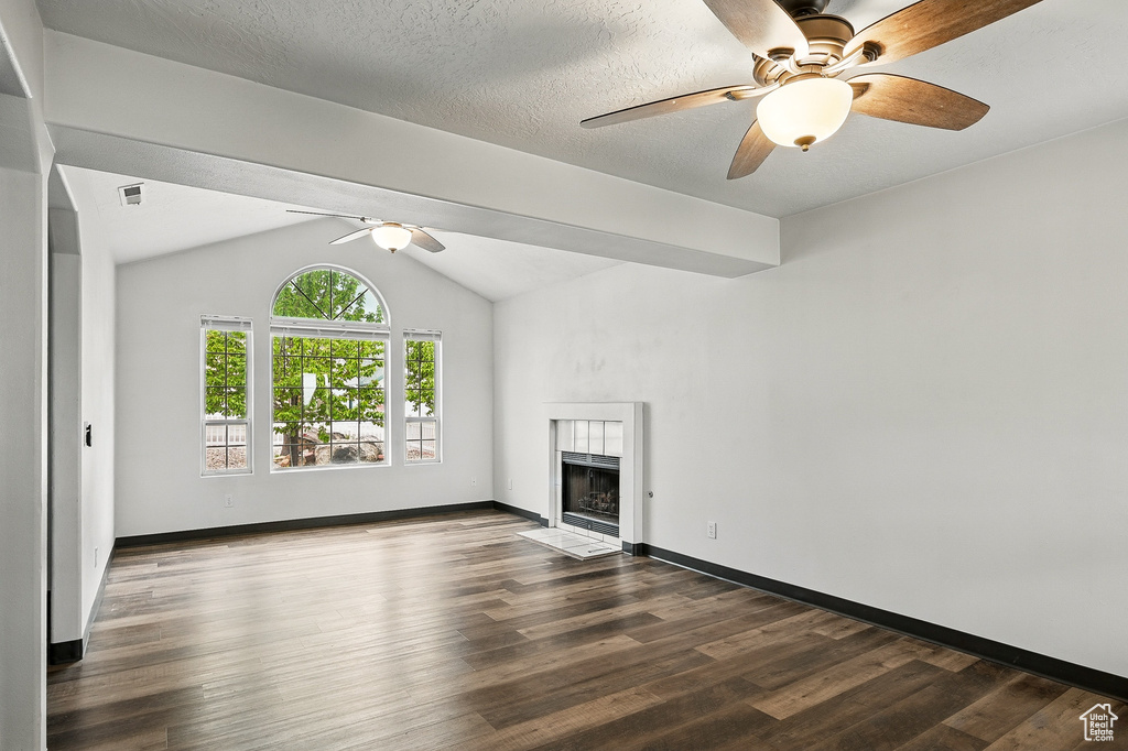 Unfurnished living room featuring a ceiling fan, a tile fireplace, dark wood-type flooring, baseboards, and vaulted ceiling