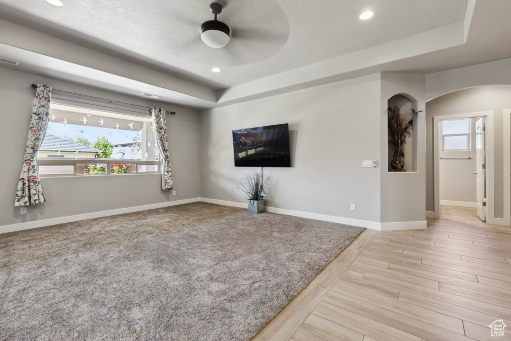 Unfurnished living room with a tray ceiling, arched walkways, recessed lighting, baseboards, and a ceiling fan