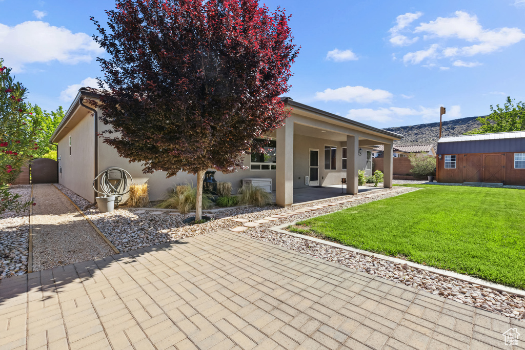 Rear view of property with a lawn, stucco siding, a patio area, and an outbuilding