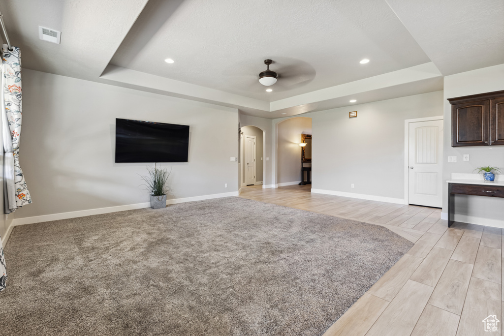 Unfurnished living room featuring a tray ceiling, a ceiling fan, arched walkways, baseboards, and recessed lighting