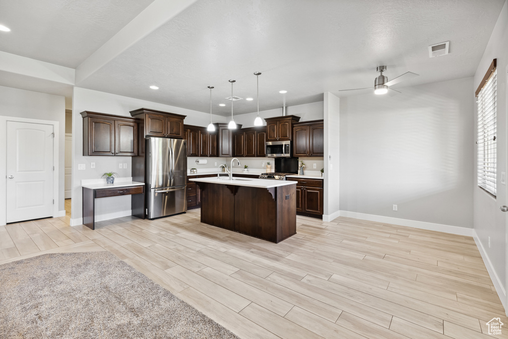 Kitchen featuring appliances with stainless steel finishes, a breakfast bar area, light countertops, baseboards, and dark brown cabinetry