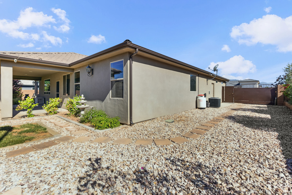 View of property exterior featuring a gate, stucco siding, central air condition unit, and fence