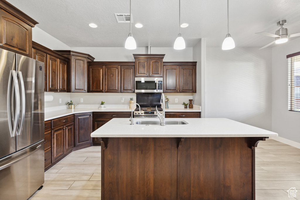 Kitchen with appliances with stainless steel finishes, light countertops, decorative light fixtures, dark brown cabinets, and recessed lighting